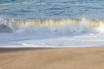 small transparent wave breaking on sandy shoreline with washback foam