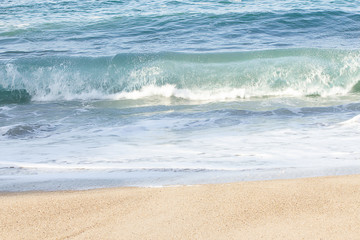 Fototapeta na wymiar small transparent wave breaking on sandy shoreline with washback foam