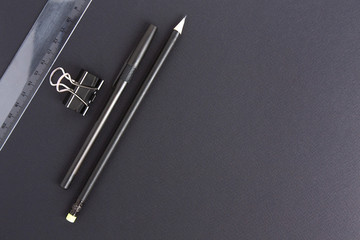 Black pen, pencil, clip and transparent ruler on a black background with a place under the text