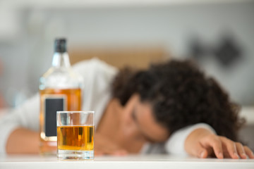 woman slumped over beside a bottle of alcohol