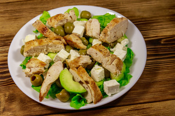 Tasty salad with fried chicken breast, green olives, feta cheese, avocado, lettuce and olive oil on wooden table