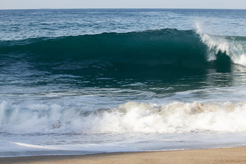 transparent tourqouise blue wave tube breaking with foam on shoreline with backspray, and backwash