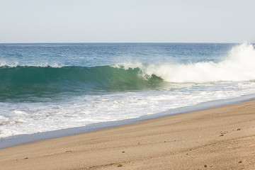 splashing wave breaking from swelling wave in froth of backwash on sandy beach