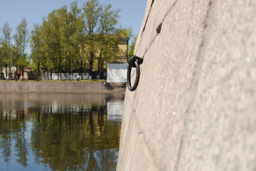 Black metal ring for mooring ships in granite slabs of the embankment of the city bay