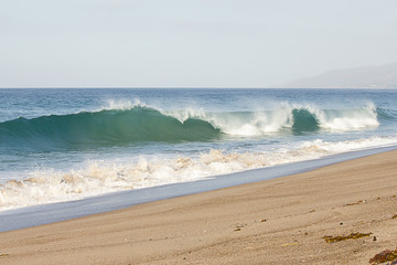 breeaking tube wave with foam creasting toward shoreline with backwash on sandy beach