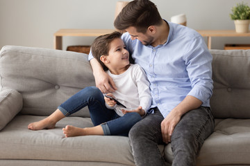 Happy dad and preschooler son relax on couch together