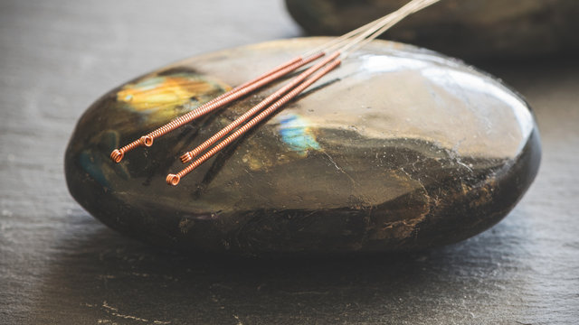 Nahaufnahme: chinesische Akupunturnadeln liegen auf einem Labradorit Heilstein, TCM