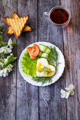 Fried eggs with lettuce, cucumber and tomato slices on wooden background