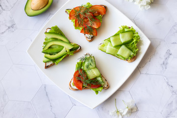 Vegetarian sandwiches with avocado, tomatoes and cucumbers on a light background