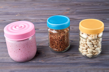 Jars of cereals on kitchen table. Glass jars with white kidney beans and raw buckwheat on wooden table. Storage of grain products.