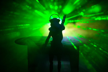 Dj club concept. Woman DJ mixing, and Scratching in a Night Club. Girl silhouette on dj's deck, strobe lights and fog on background. Creative artwork decoration with toy.