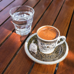Traditional strong and dark Turkish coffee served with a glass of water on a side on a wooden table in  outdoor cafe