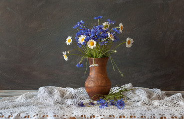 Still life in a rustic style. A bouquet of wildflowers in a clay pitcher  on the table. Daylight.