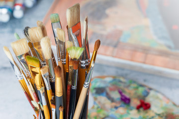 Fototapeta premium Paint brushes in a glass close-up on the background of a palette, paints and canvas.