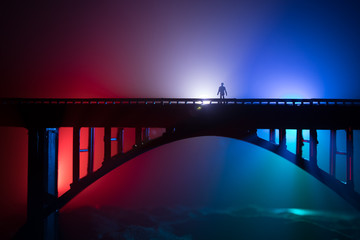 Artwork decoration. Silhouette of powerful metallic bridge at night with foggy backlight. Silhouette of person standing on bridge.