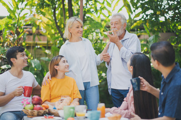 Happy big family have a lunch at outdoor in green garden. Lunch or tea time on picnic table in summer. Big family outdoor lunch concept.