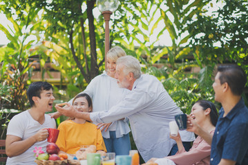 Happy big family have a lunch at outdoor in green garden. Lunch or tea time on picnic table in summer. Old man give a bread to young man  Big family outdoor lunch concept.