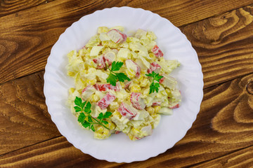 Salad with crab sticks, sweet corn, chinese cabbage, eggs and mayonnaise on wooden table