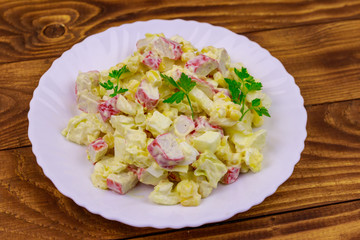 Salad with crab sticks, sweet corn, chinese cabbage, eggs and mayonnaise on wooden table