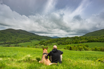 Fototapeta na wymiar Active man sitting with dog in mountains, looking at view ad resting