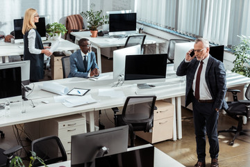 overhead view of businessman talking on smartphone near multicultural coworkers in office