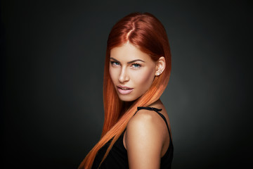 Beauty portrait of a red-haired woman with blue eyes in a studio on a dark background