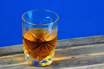 Alcoholic drink in a glass on a wooden table top, blue background. Strong aromatic alcoholic drink, from different types of grain - whiskey or Bourbon. Cognac or brandy - from grape must.