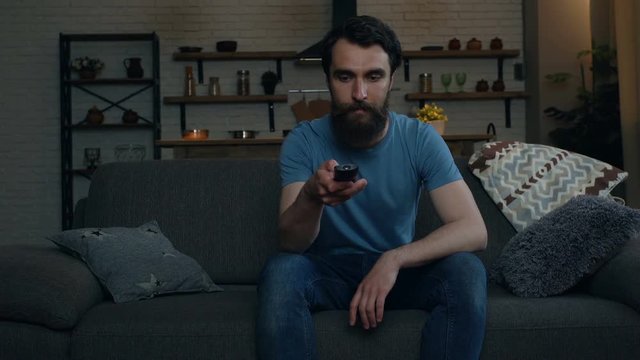 Young man sitting on the sofa, taking remote control tv and turn on TV.
