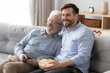Happy millennial son and elderly dad have fun watching movie