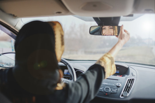 Gorgeous muslim woman adjusting rearview mirror in her car.