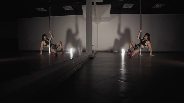 Beautiful woman pole dancing at dark studio with mirror. Close up of woman with sexy shape is dancing near the pole in slow motion. Dancer moving with pylone
