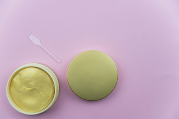 Hydrogel cosmetic eye patch jar with golden patches against dark circles under eyes with spoon. Beauty health care concept. Flat lay set on pink background. 