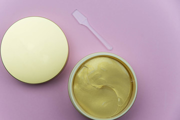 Hydrogel cosmetic eye patch jar with golden patches against dark circles under eyes with spoon. Beauty health care concept. Flat lay set on pink background. 