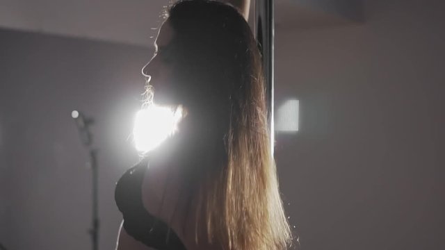 Close-up of woman with sexy shape is dancing near the pole in slow motion. Young sexy woman pole dancing at dark studio with mirror. Dancer moving with pylone. Wide angle