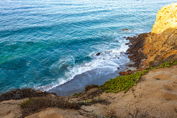 clff side view of pacific ocean wavy shore and rocks, from sandy iceplant edged path