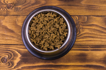 Dry cat food in bowl on wooden background. Pet food on wood surface. Top view