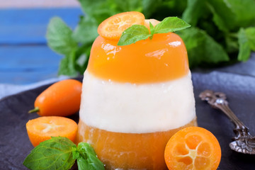Layered dessert with fruits and yogurt on the black plate surrounded by kumquats and mint