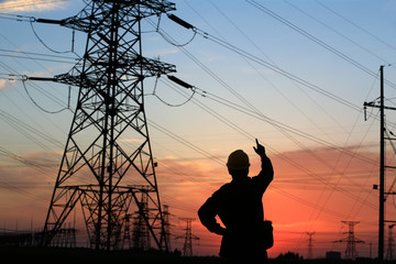 A silhouette of a man in front of a high voltage tower