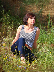Middle aged woman sitting in long dry summer grass.