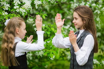 Obraz premium Little girls in stylish school uniforms play outdoors in the blossoming apple park
