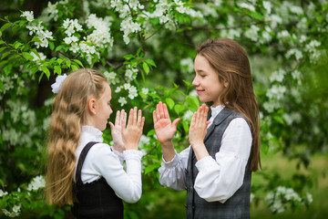 Obraz premium Little girls in stylish school uniforms play outdoors in the blossoming apple park