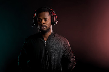 Beautiful African American man listening to sad music through headphones on black