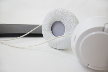 White headphones and black phone on a light background.