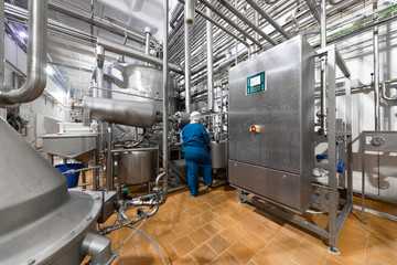 worker in a blue robe and a cap inspect the production department of dairy factory