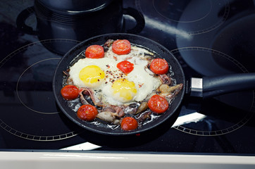scrambled eggs cooking in a frying pan, cooking on a ceramic stove, fried eggs with bacon and tomato, top view closeup