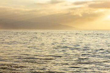 open ocean expanse at sunrise, with clouds, sunrays, water texture, and distant hills,
