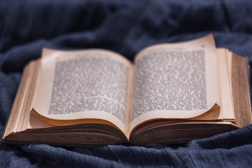 open book on blue background, texture blue fabric, old book, curled corners, blurred text