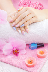 Obraz na płótnie Canvas beautiful colored manicure with decor, orchid, towel and candle on the white wooden table. spa