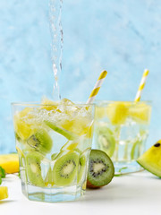 Cool soda water pouring into yellow watermelon and kiwi lemonade with ingredients on bright blue background. Vegetarian food concept. Detox