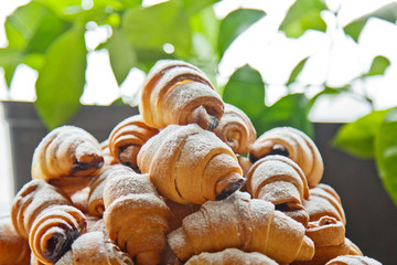 Buns in a plate full of freshly baked bagels sprinkled with powdered sugar on the kitchen table. cooking baking. croissants baking preparation stage. breakfast closeup copy space